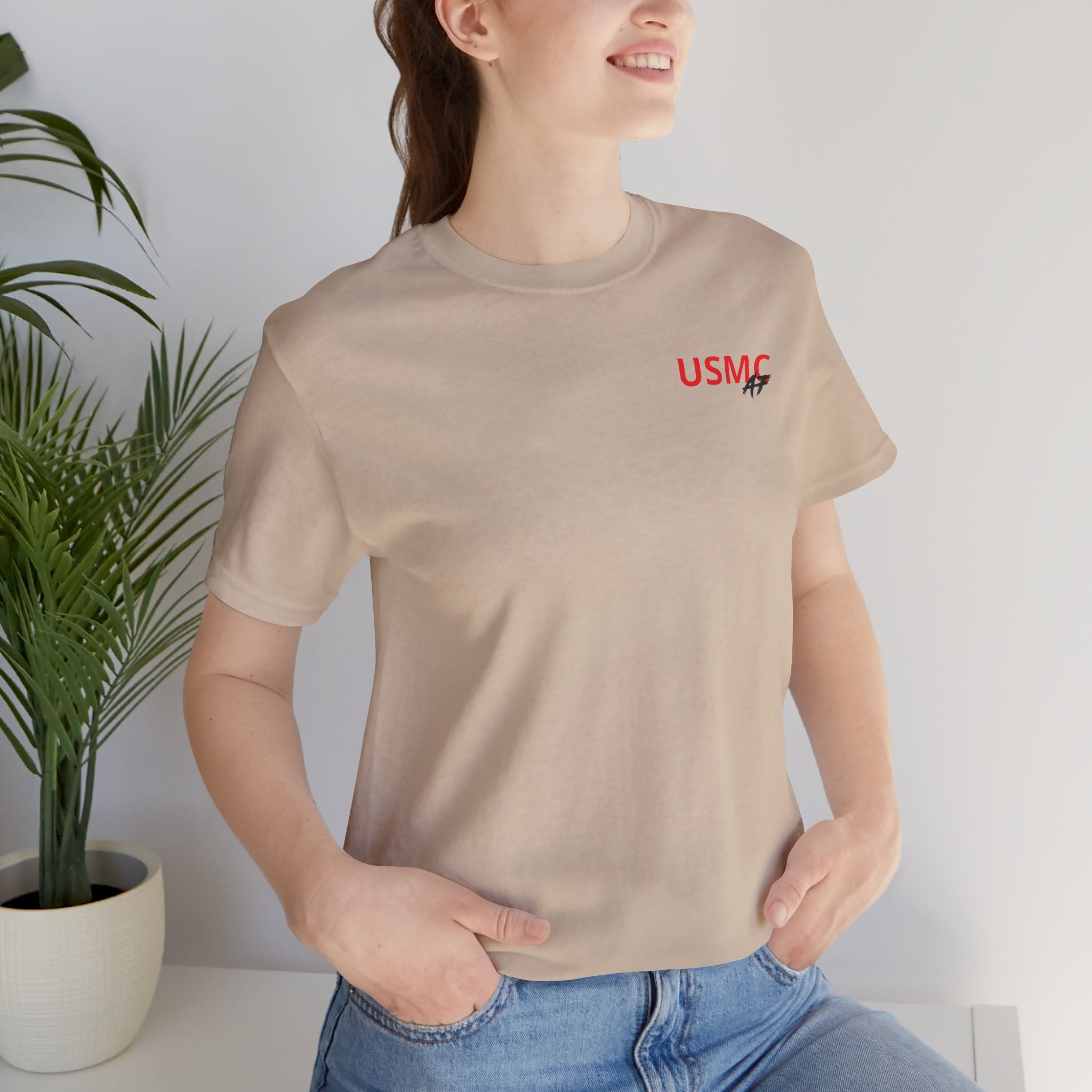Woman wearing the Marine Corps veteran T-shirt in Tan beside a potted plant