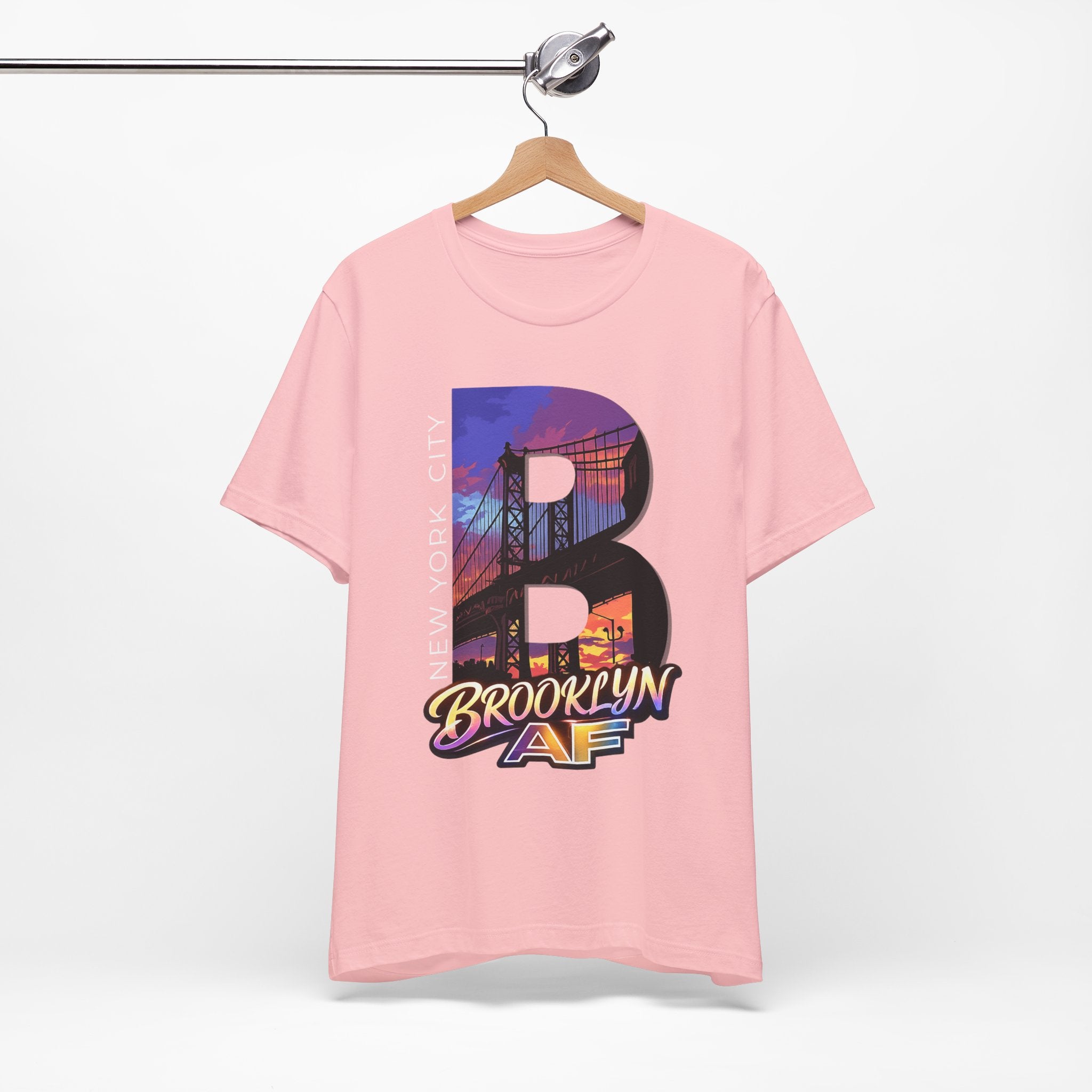 Pink t-shirt on a hanger, front view showing the full 'B' Brooklyn Bridge sunset skyline graphic and 'Brooklyn AF' logo