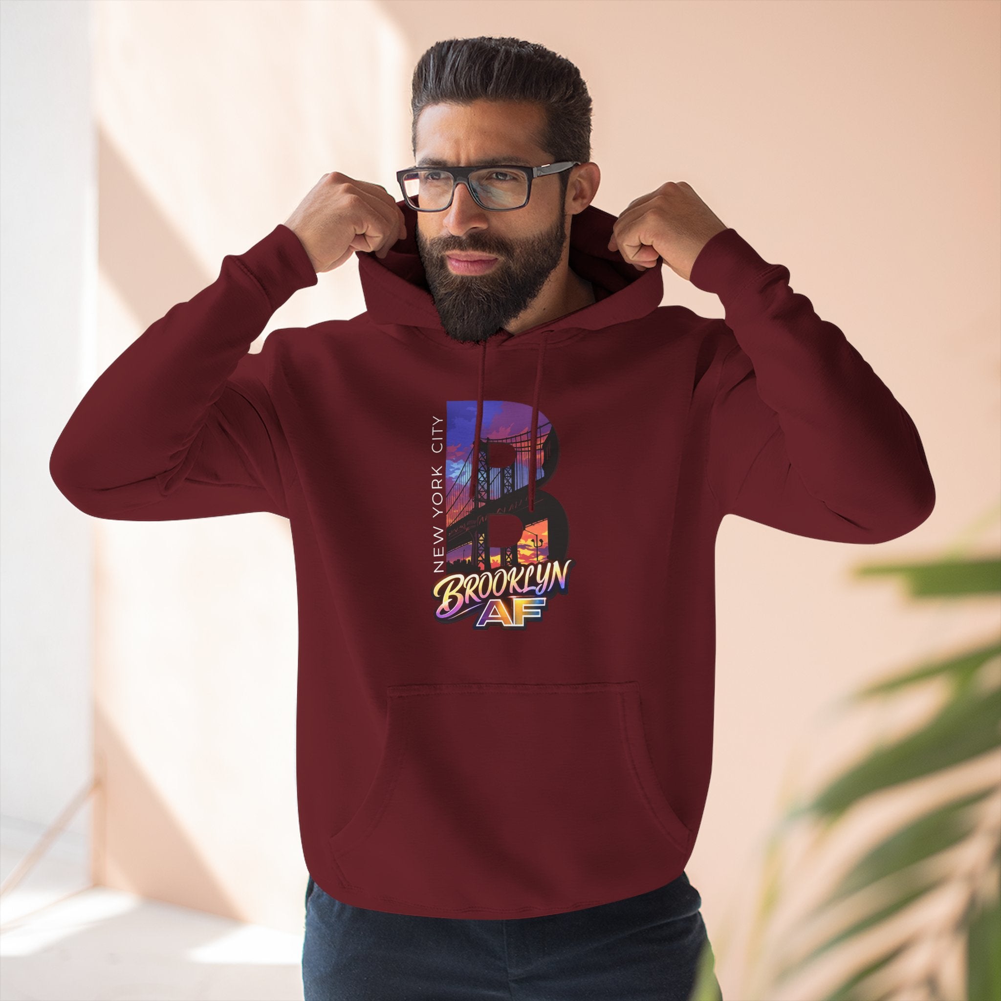 Maroon hoodie worn by a model, close-up view, adjusting the hood, with the oversized B skyline graphic visible.