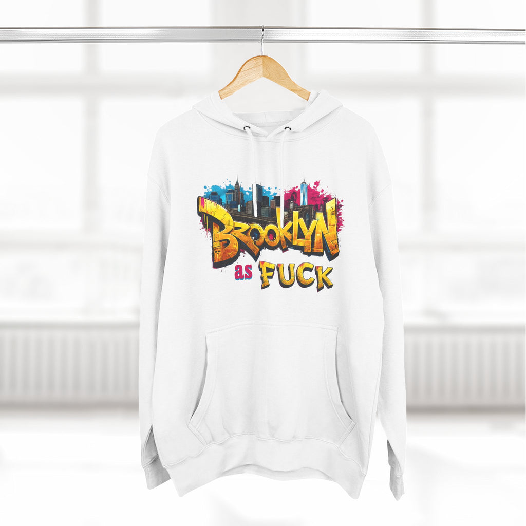White Brooklyn As Fuck hoodie on a wooden hanger, front view, with graffiti-style lettering and a colorful NYC skyline print.