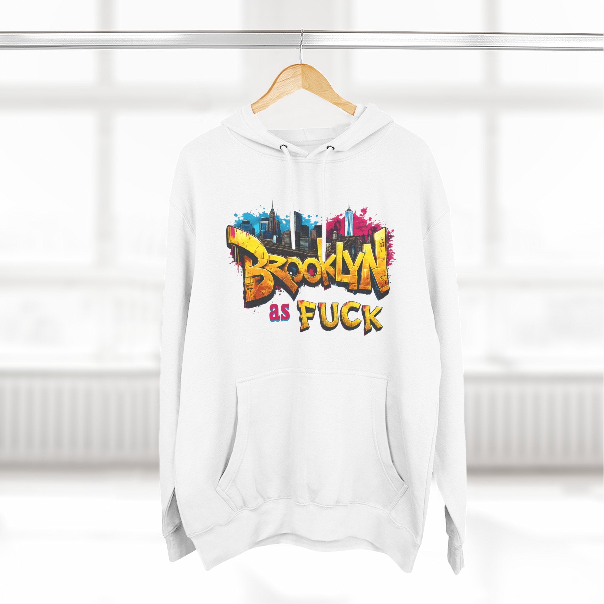 White Brooklyn As Fuck hoodie on a wooden hanger, front view, with graffiti-style lettering and a colorful NYC skyline print.