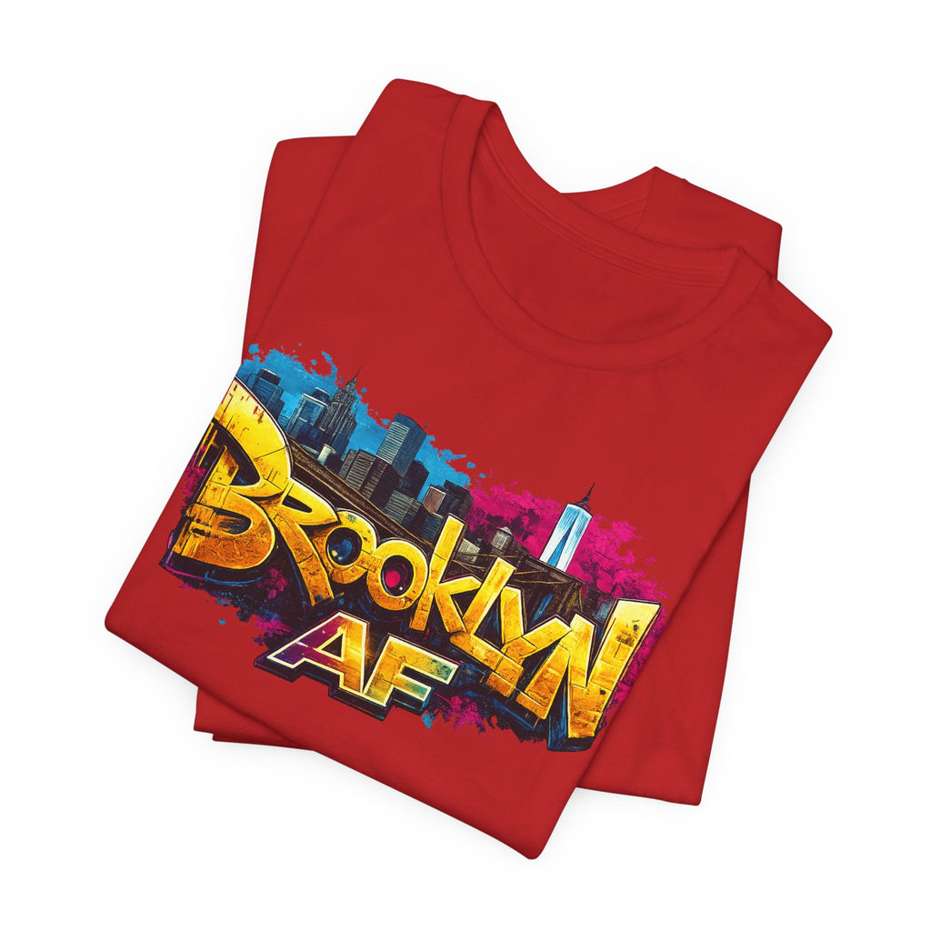 Red t-shirts folded in a stack, featuring graffiti-style Brooklyn AF lettering over a skyline paint-splash design.