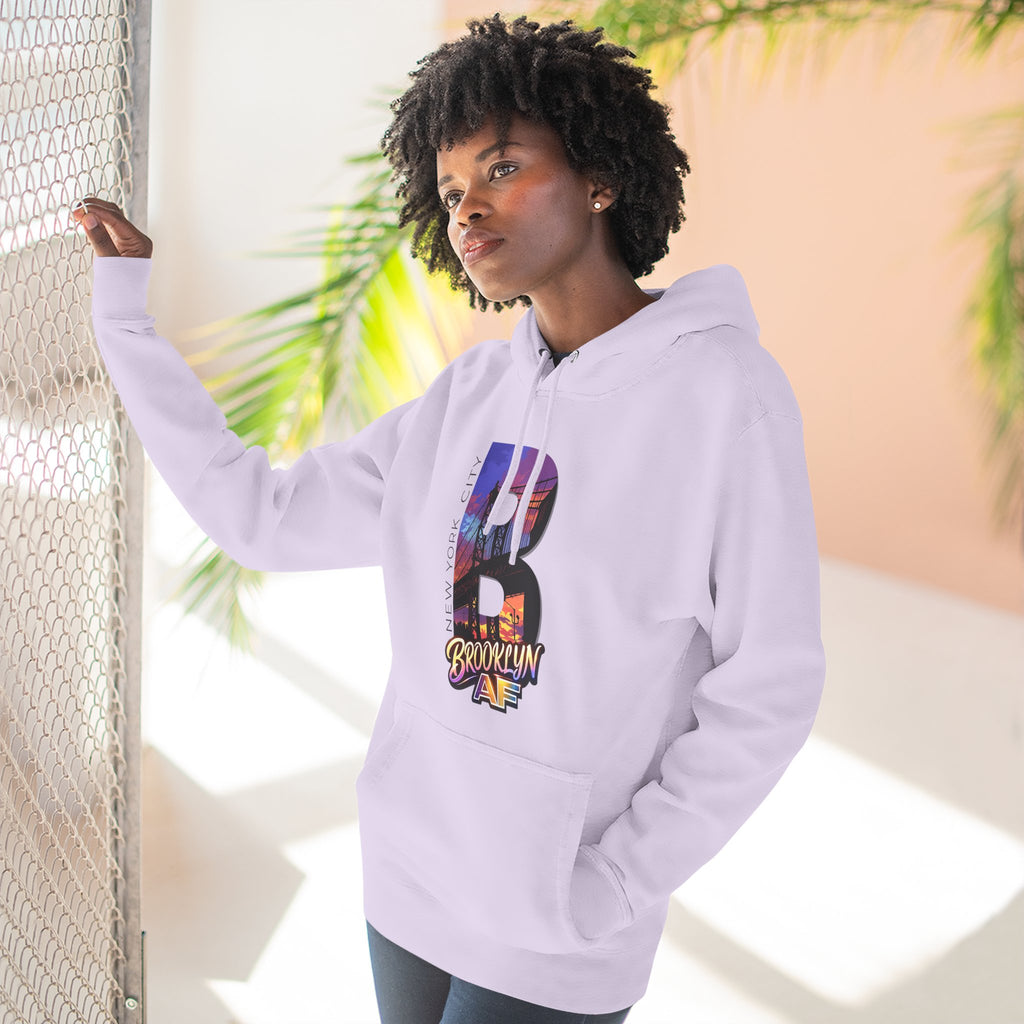 Lilac hoodie worn by a model against a window, oversized B with a Brooklyn Bridge sunset skyline graphic.