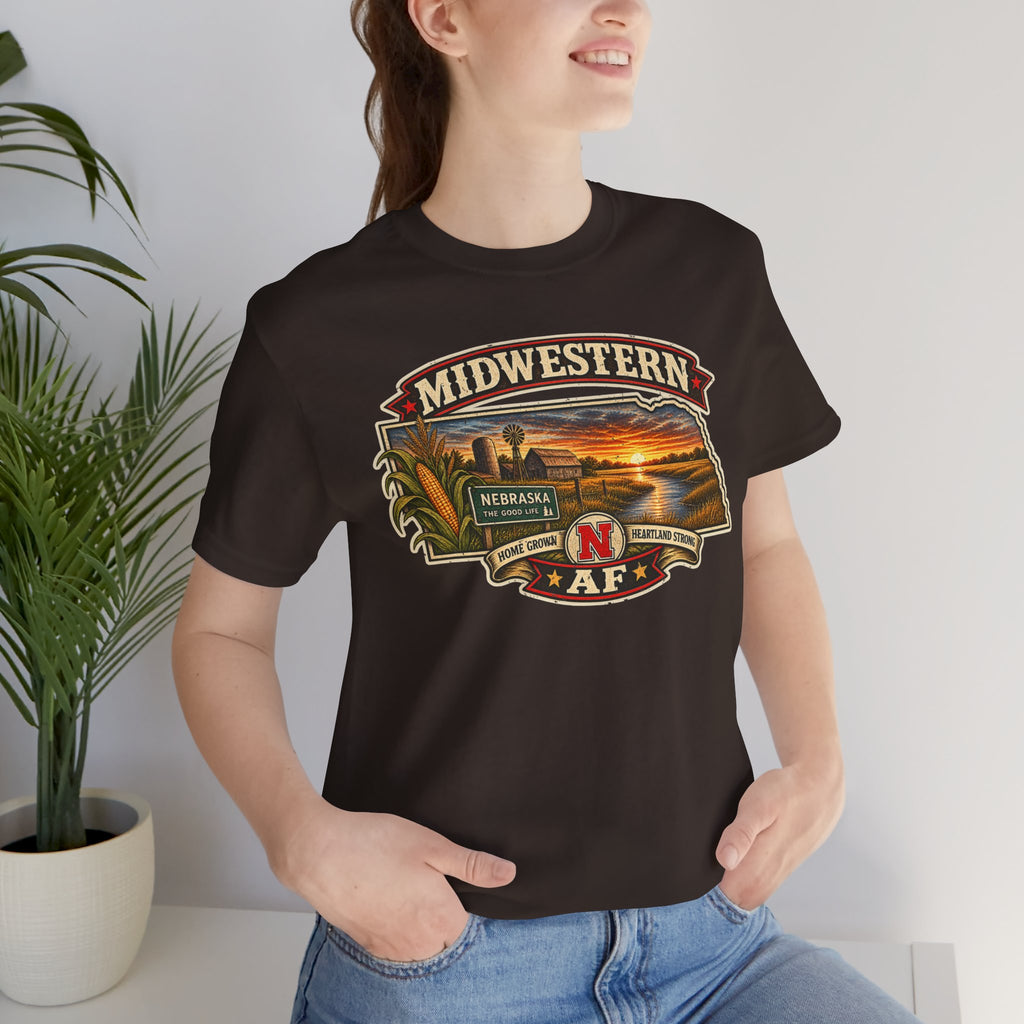 Woman in the brown Nebraska tee indoors, front print showing the Nebraska sunset badge