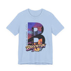 Light blue t-shirt, flat lay, with a bold oversized "B" featuring a Brooklyn Bridge sunset skyline graphic.