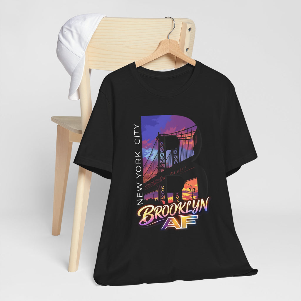 Black t-shirt hanging on a wooden chair with a white cap, purple-orange Brooklyn Bridge sunset B graphic.