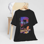 Black t-shirt hanging on a wooden chair with a white cap, purple-orange Brooklyn Bridge sunset B graphic.