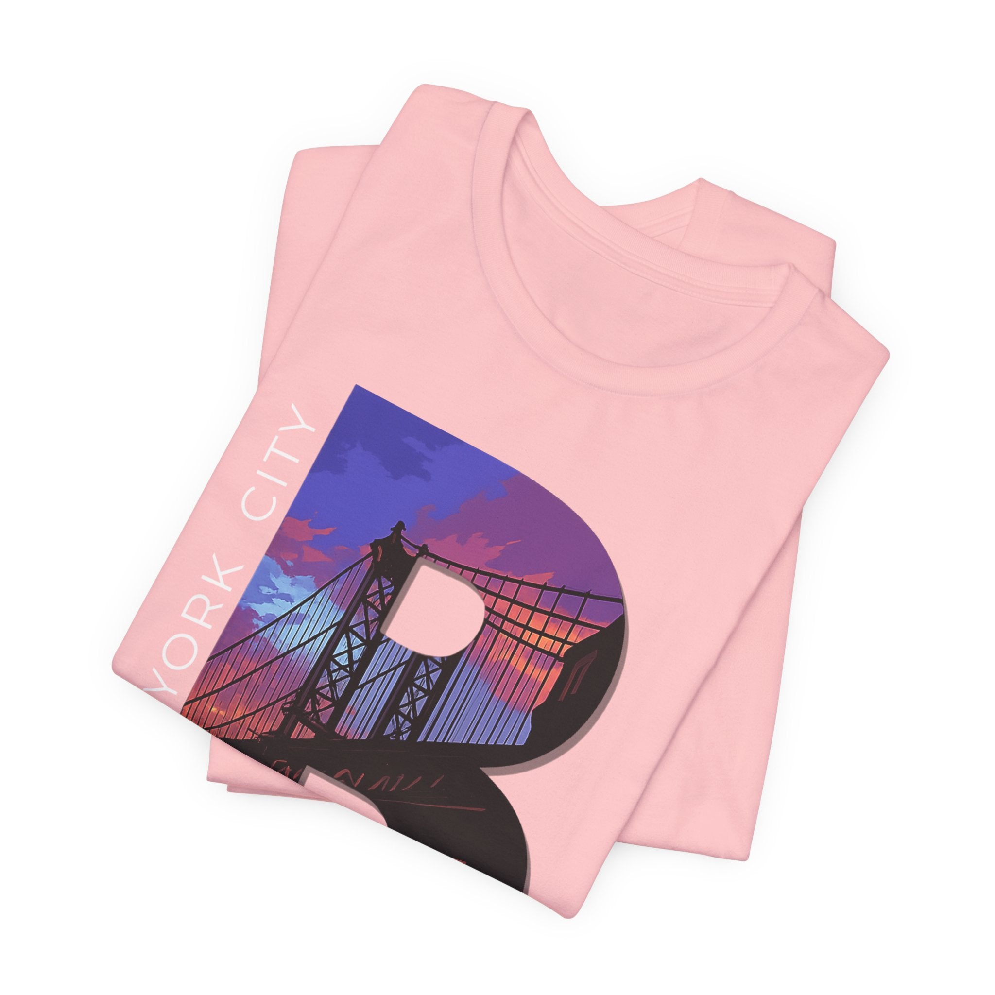 Pink t-shirt folded in a stack, close-up of the oversized 'B' with Brooklyn Bridge sunset skyline graphic