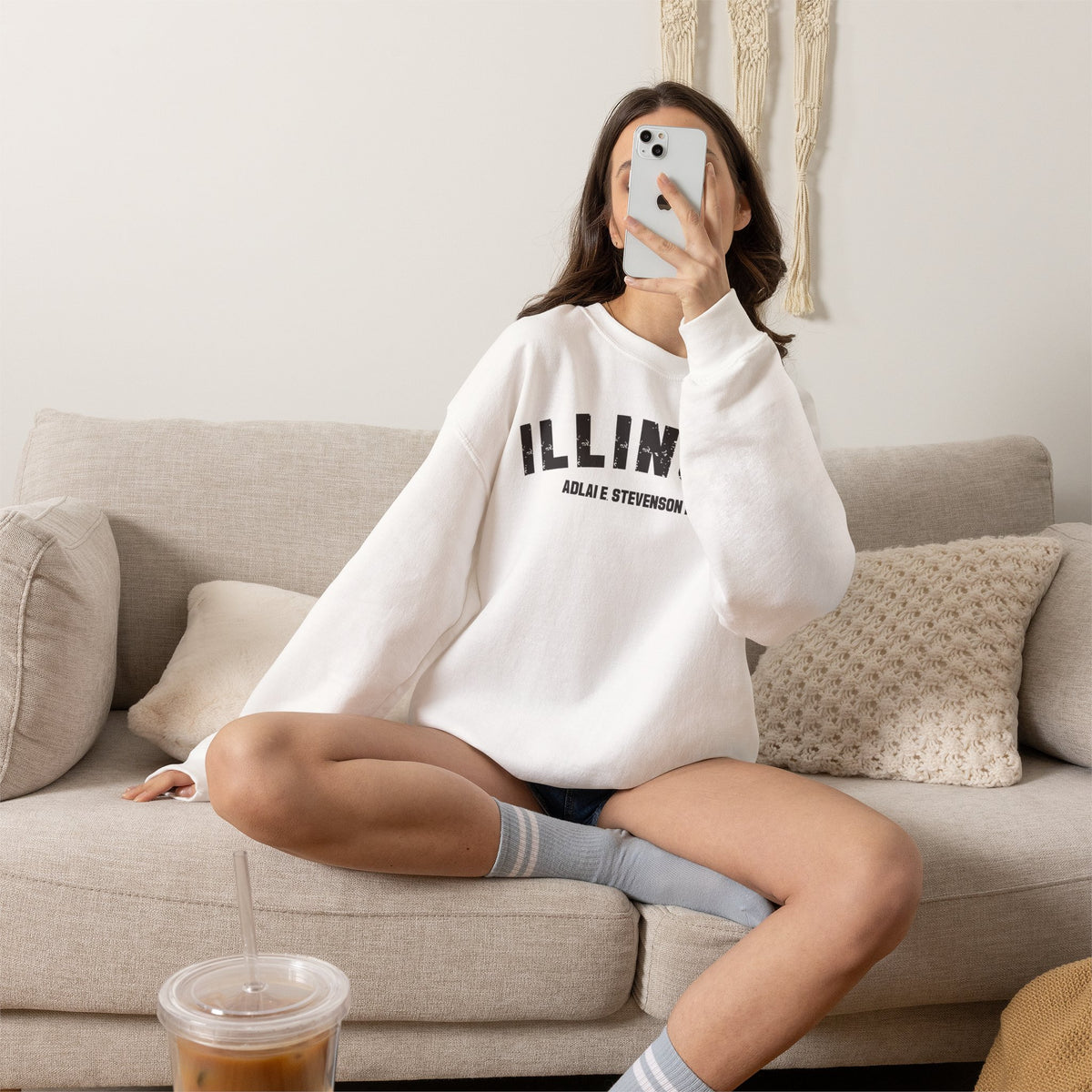 Woman on a couch in a White custom Illinois sweatshirt, charcoal varsity ILLINOIS above a school name
