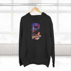 Black hoodie hanging on a wooden hanger by a blurred window, featuring the oversized "B" Brooklyn Bridge skyline graphic.