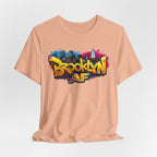 Heather Peach t-shirt, front view flat lay, showing graffiti Brooklyn AF lettering over a skyline paint splash.