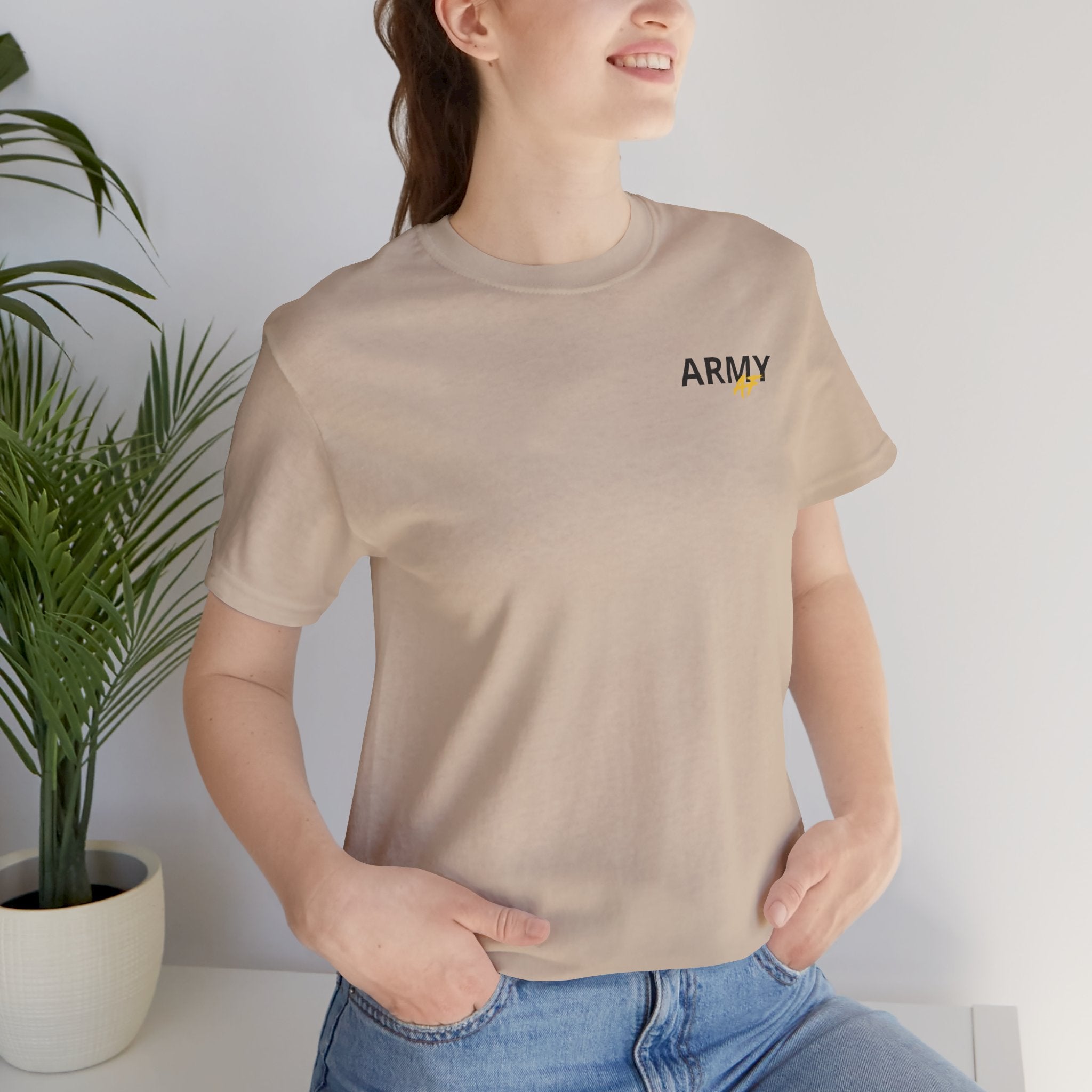 Woman wearing the Army veteran T-shirt in Tan beside a potted plant