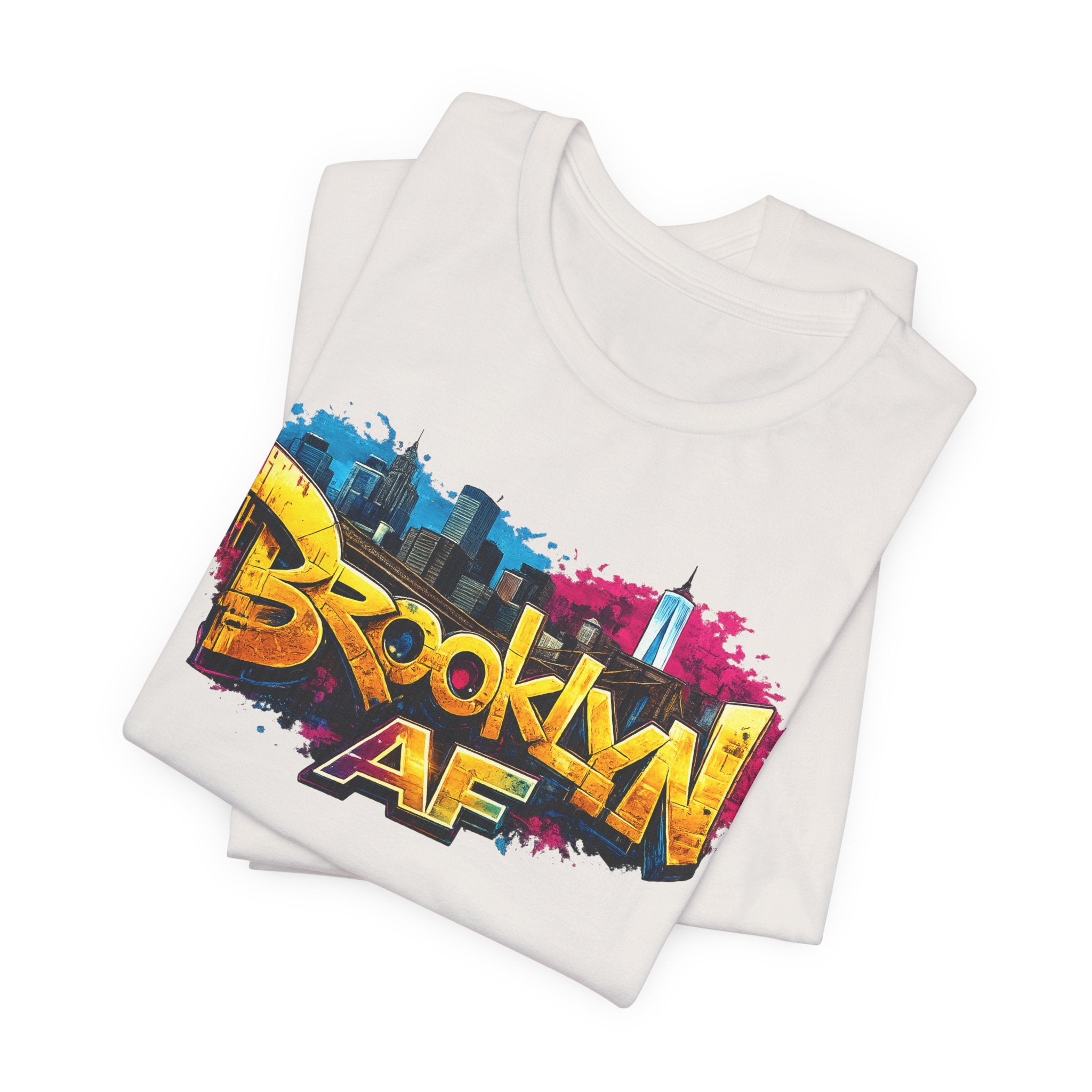 White t-shirts folded in a stack, showing graffiti-style Brooklyn AF lettering over a skyline paint splash.