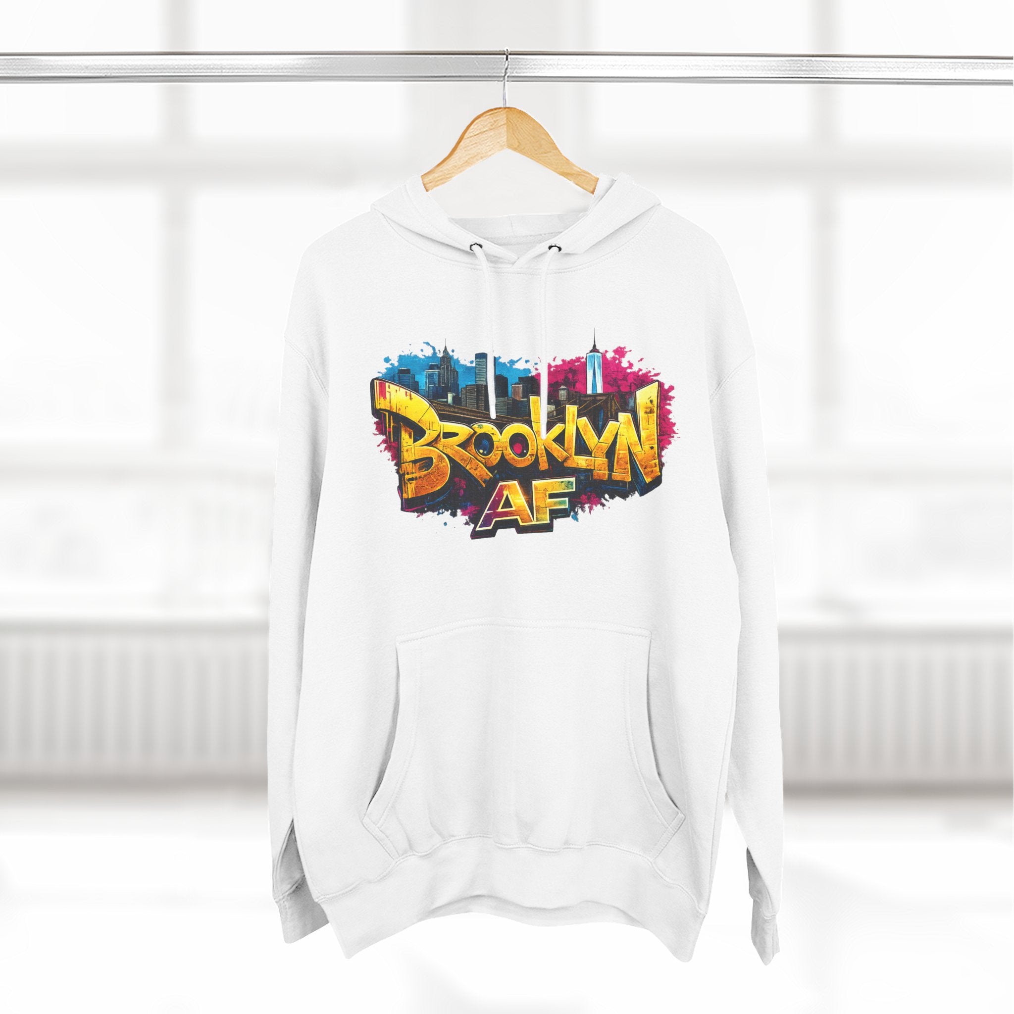 White hoodie hanging on a wooden hanger, showing the colorful graffiti-style Brooklyn AF skyline print.