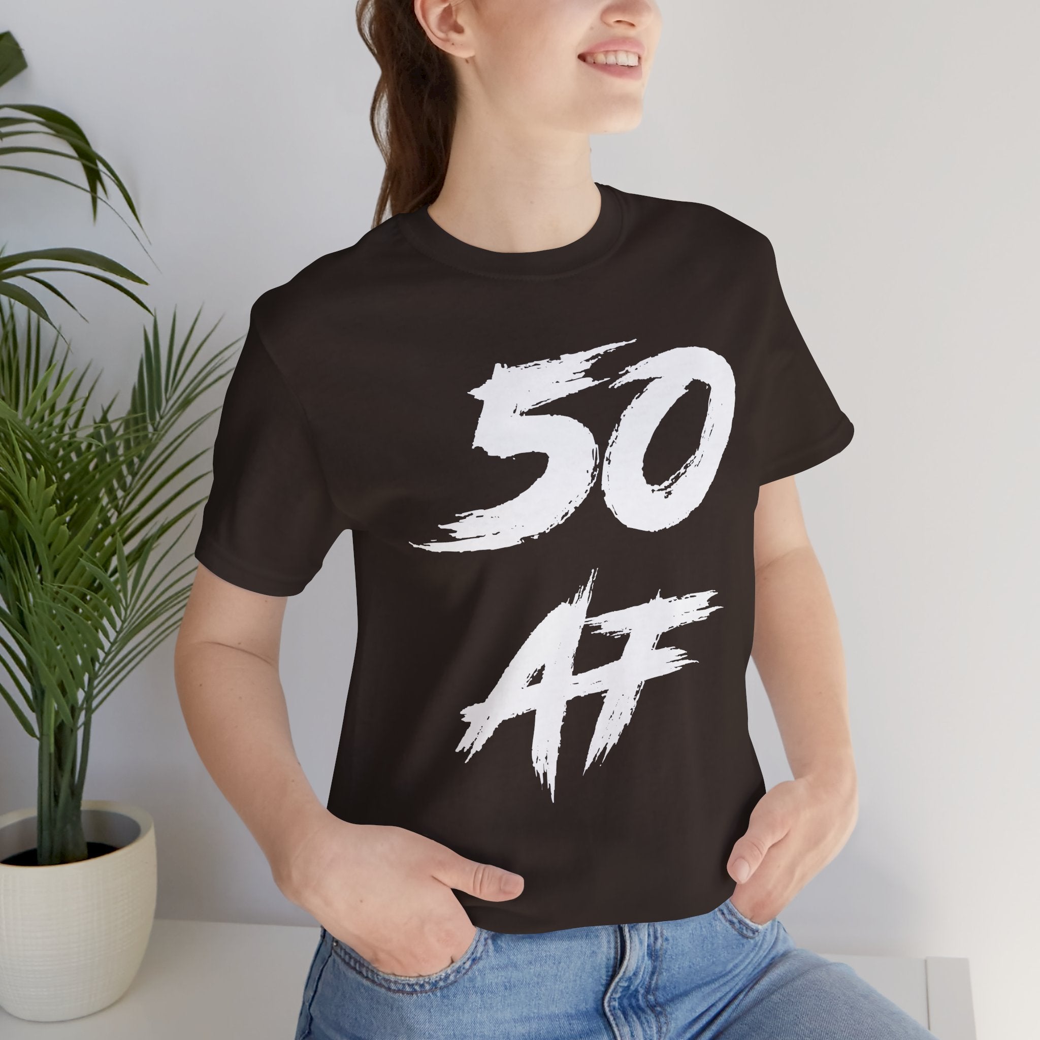 Woman indoors beside a houseplant wearing the brown 50 AF birthday tee
