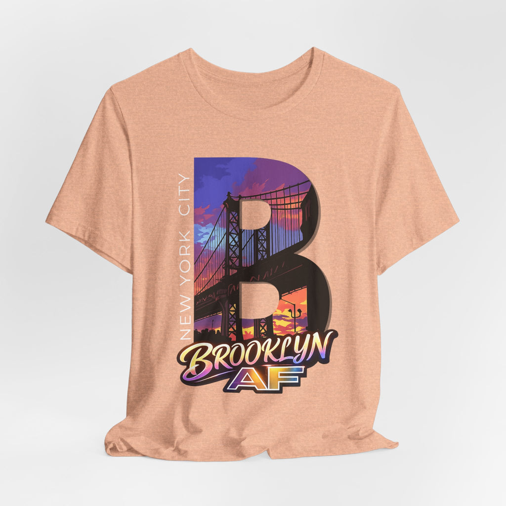Heather peach t-shirt, flat lay front view, with a bold B and a purple-orange Brooklyn Bridge sunset skyline graphic.
