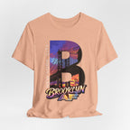 Heather peach t-shirt, flat lay front view, with a bold B and a purple-orange Brooklyn Bridge sunset skyline graphic.