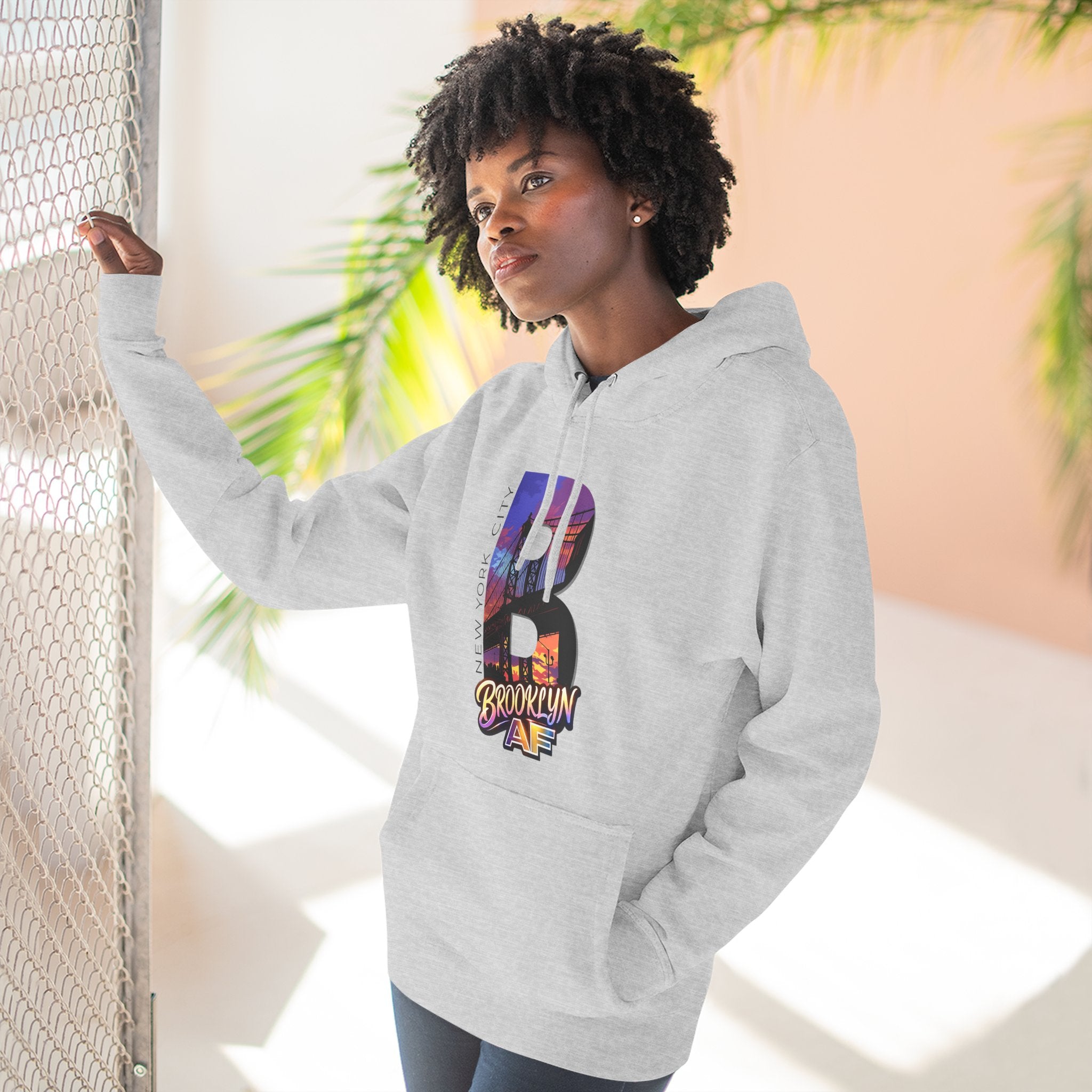 Heather grey hoodie worn by a model against a window, oversized B with a Brooklyn Bridge sunset skyline graphic.