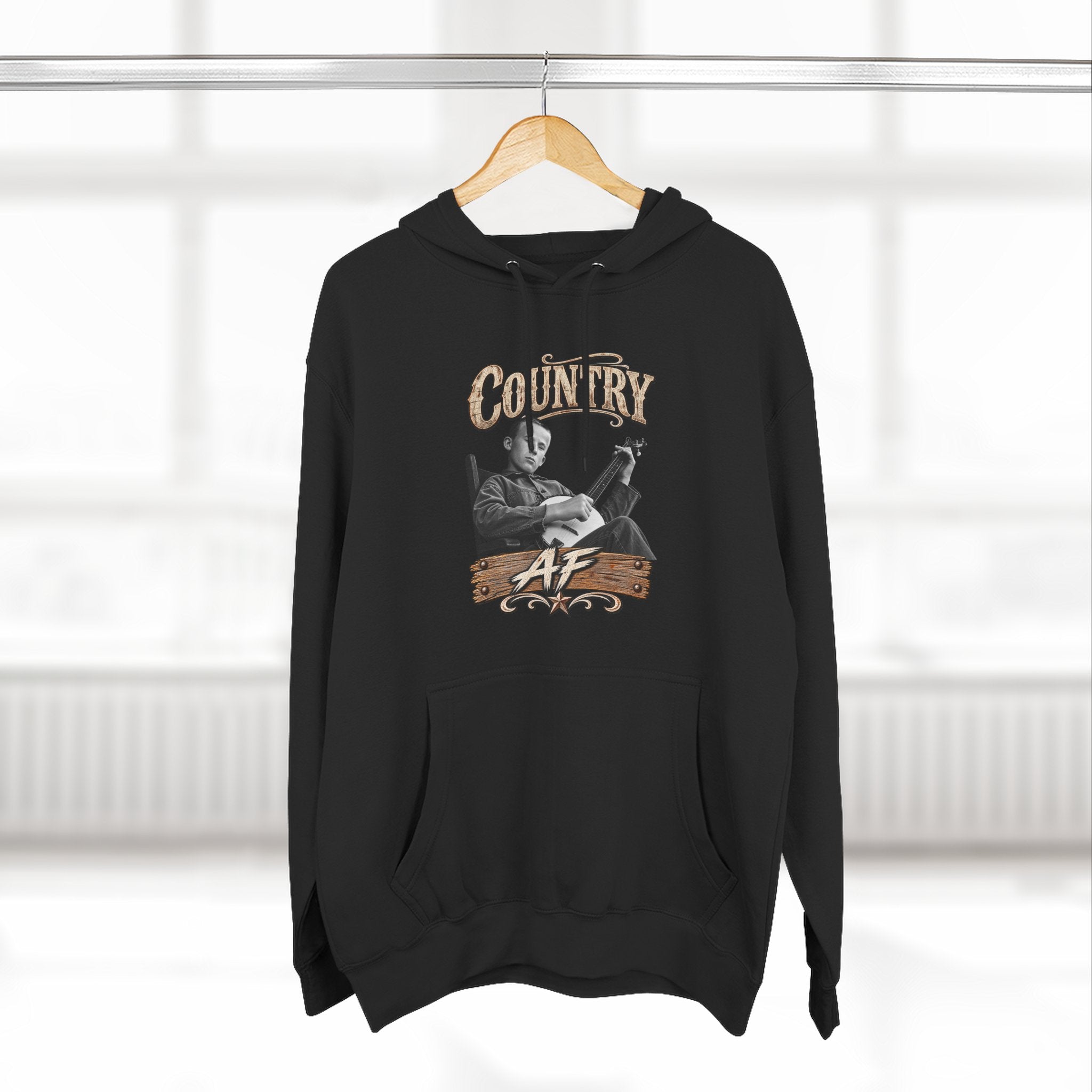 Black Country AF hoodie on a wooden hanger by a window