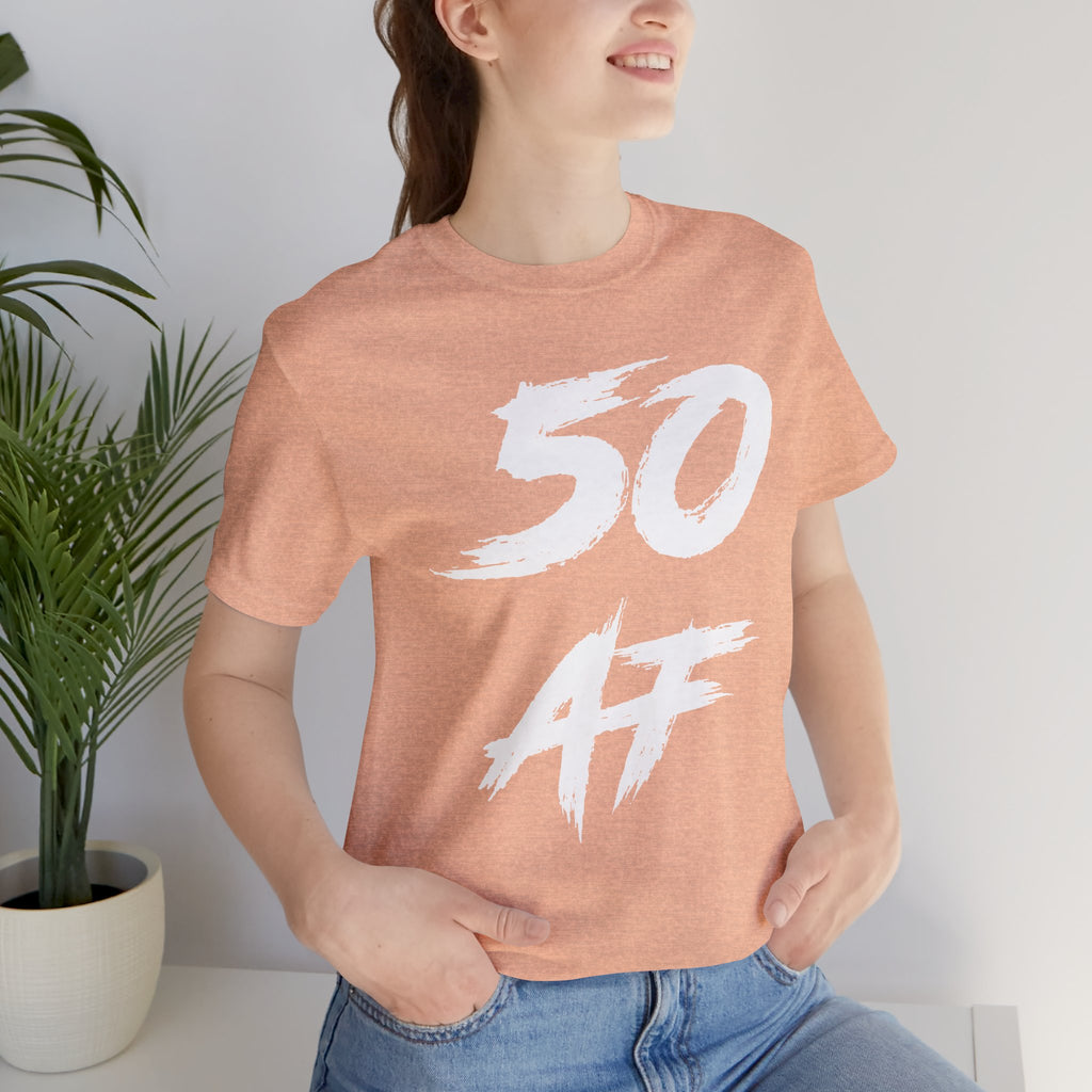Woman in the Heather Peach 50 AF birthday tee, photographed indoors by a plant