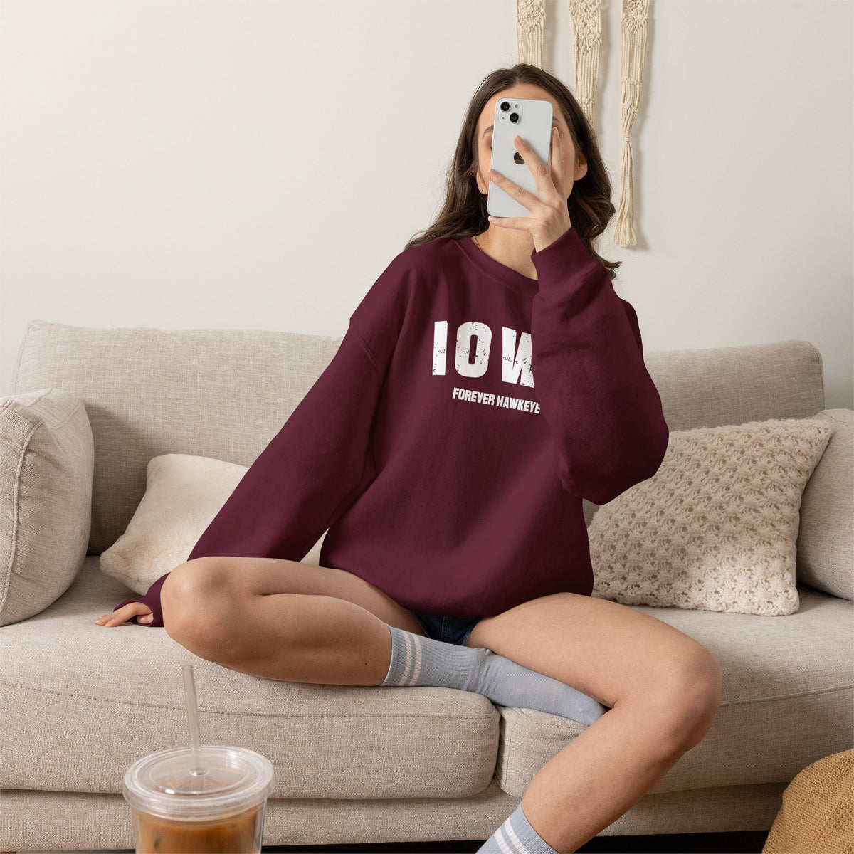 Woman on a sofa in the maroon custom Iowa crewneck with varsity IOWA and FOREVER HAWKEYE