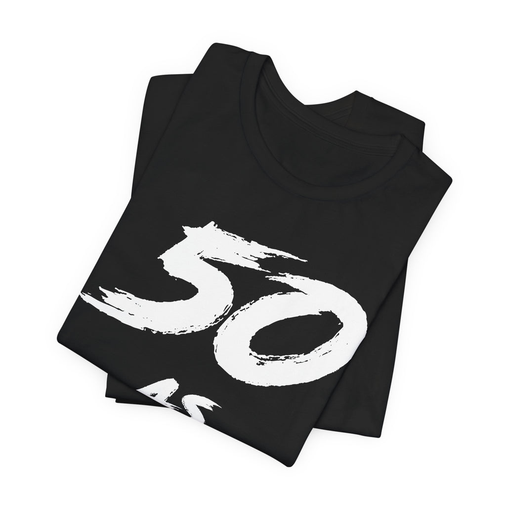Folded black birthday tees stacked, the white 50 print filling the top fold