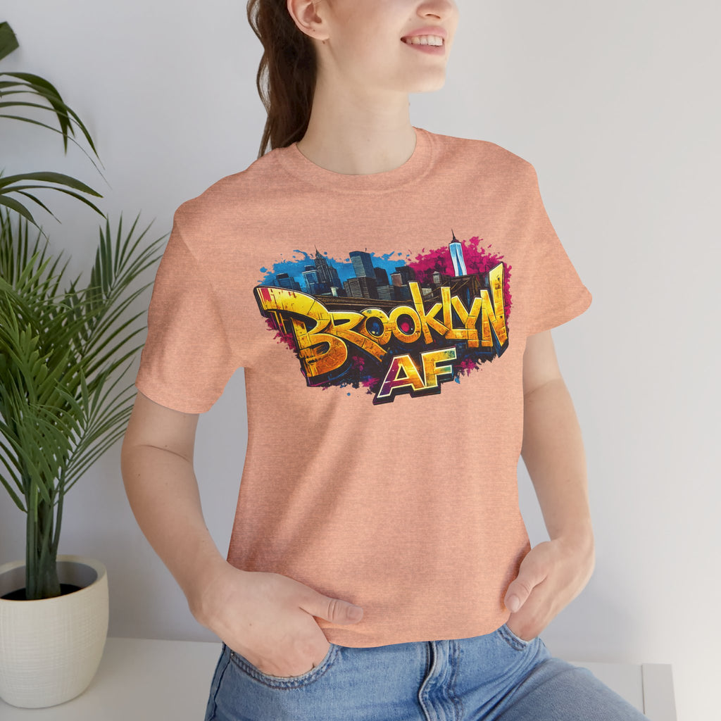 Heather Peach t-shirt worn by a model, close-up of chest print showing graffiti Brooklyn AF lettering and skyline art.