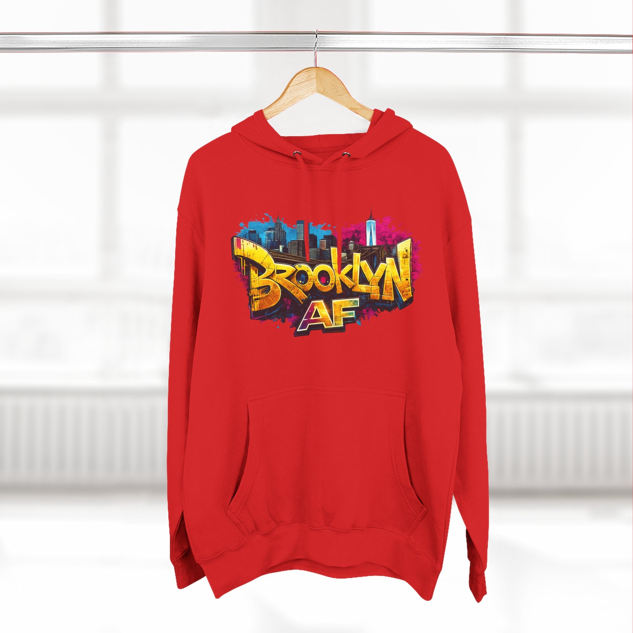 Red hoodie hanging on a wooden hanger, showing the colorful graffiti-style Brooklyn AF skyline print.