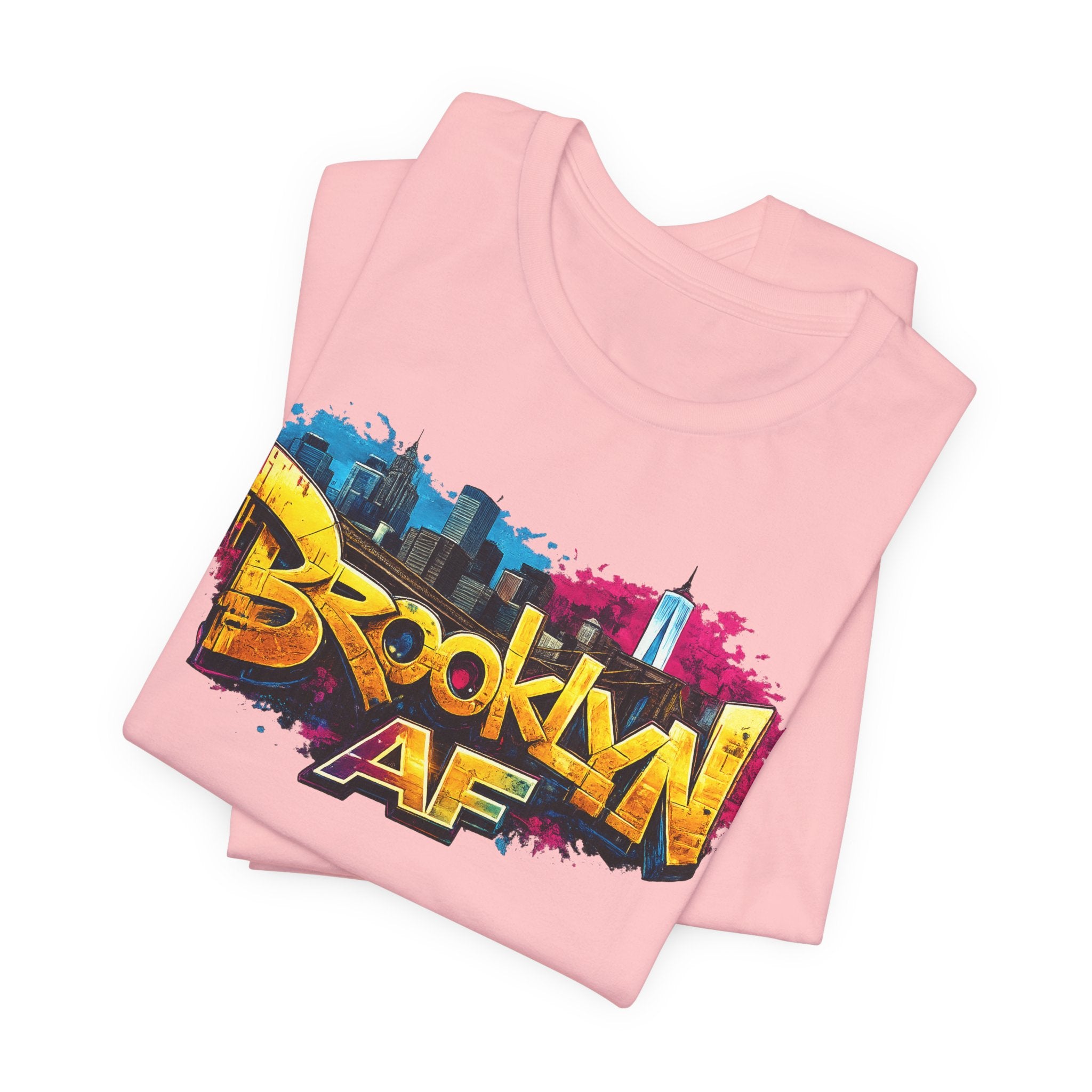 Pink t-shirts folded in a stack, featuring graffiti Brooklyn AF lettering over a skyline paint-splash design.