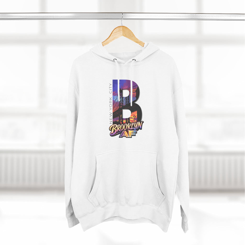 White hoodie on a wooden hanger, front view, oversized B containing a Brooklyn Bridge sunset skyline graphic.