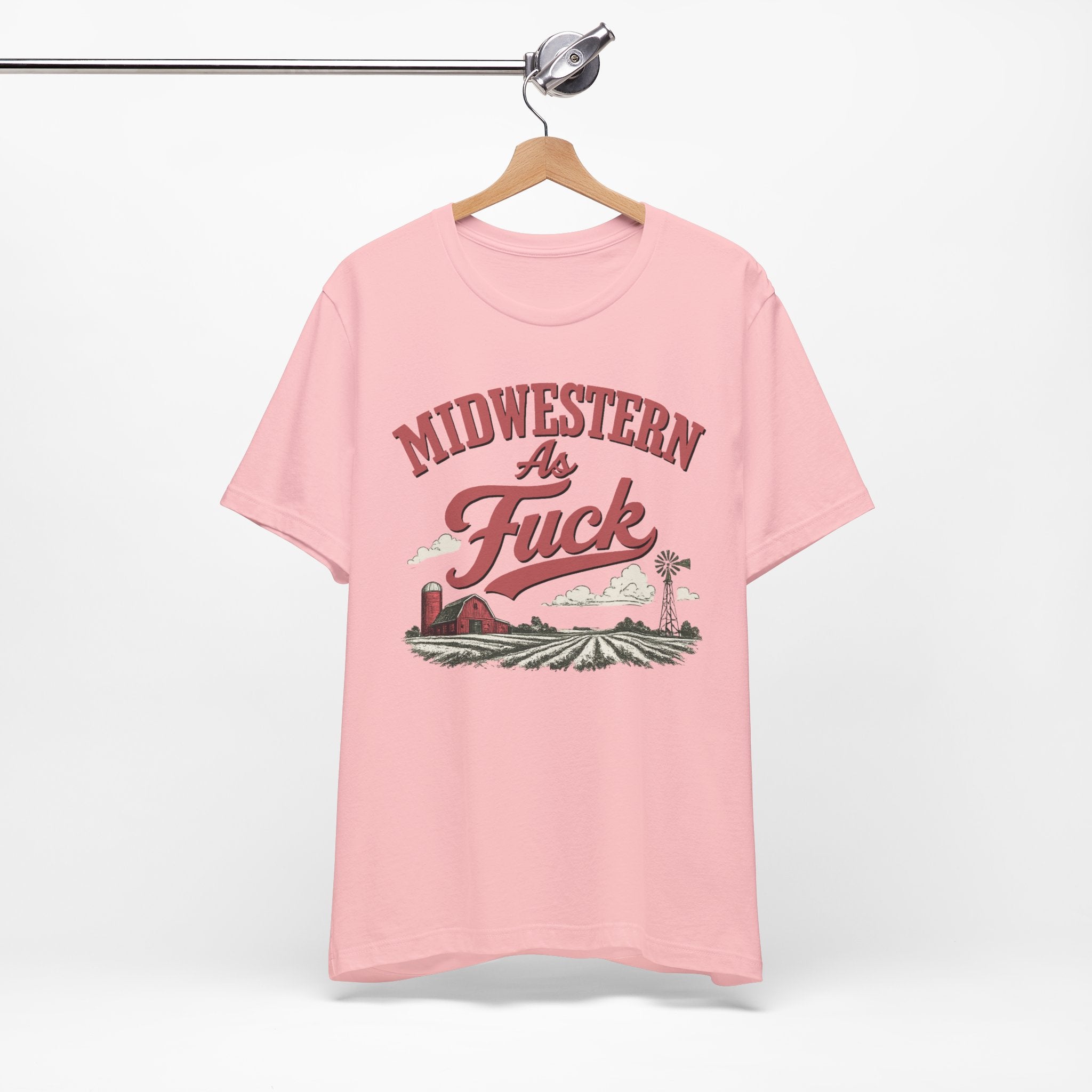 Pink Midwestern As Fuck t-shirt on a wooden hanger, front view showing the full vintage farm graphic.