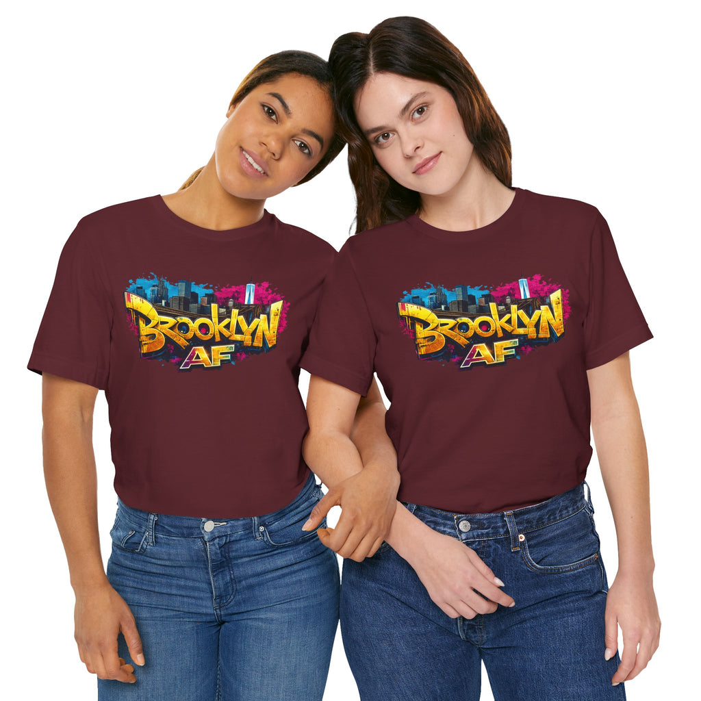 Maroon t-shirts worn by two female models, front view, featuring graffiti-style Brooklyn AF lettering over a skyline.