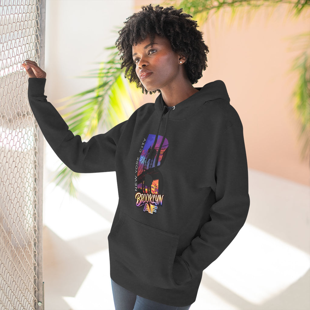 Black hoodie worn by a female model outdoors, side view with hand on a fence, oversized "B" skyline graphic on chest.