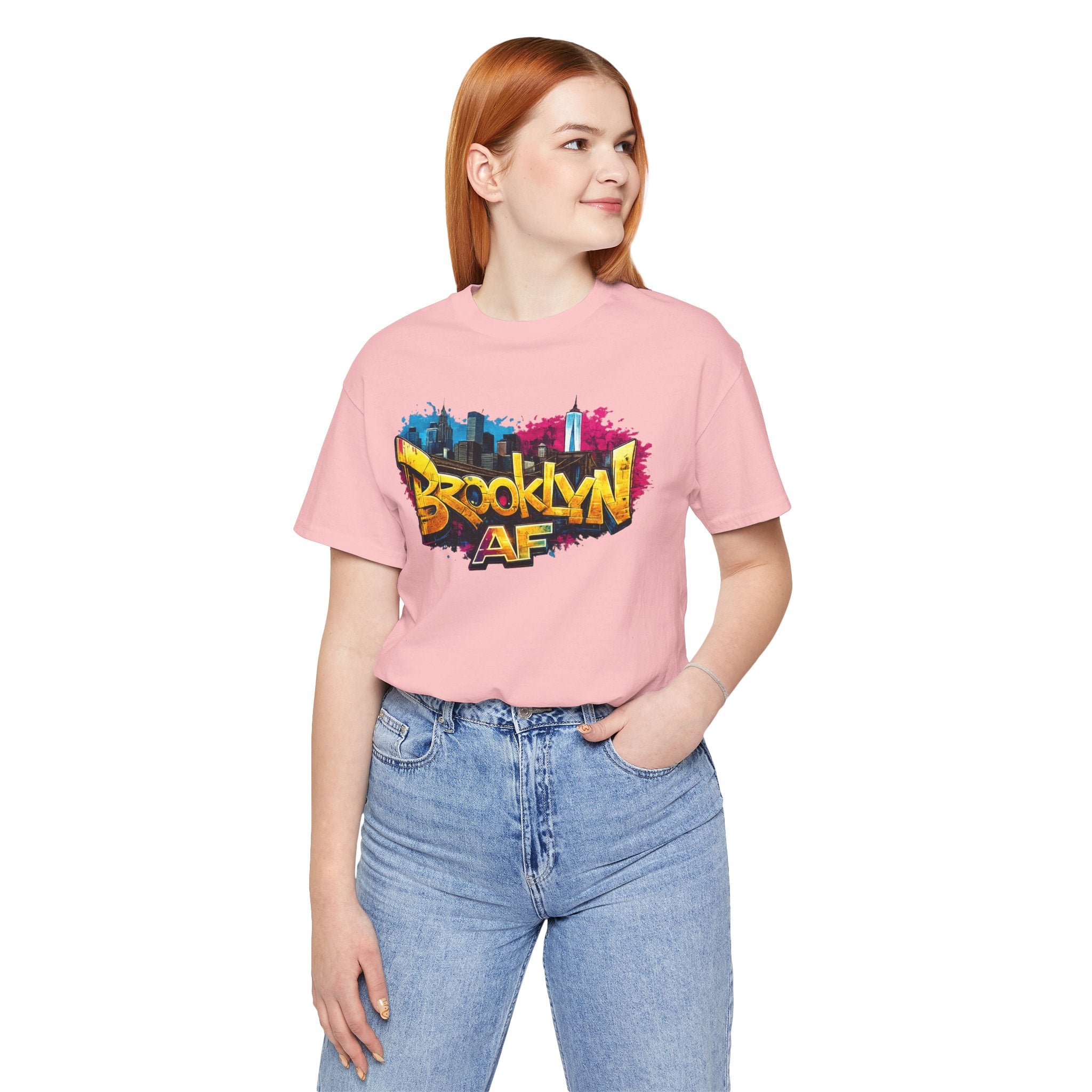 Pink t-shirt worn by a female model, front view, showing graffiti-style Brooklyn AF lettering over a skyline.