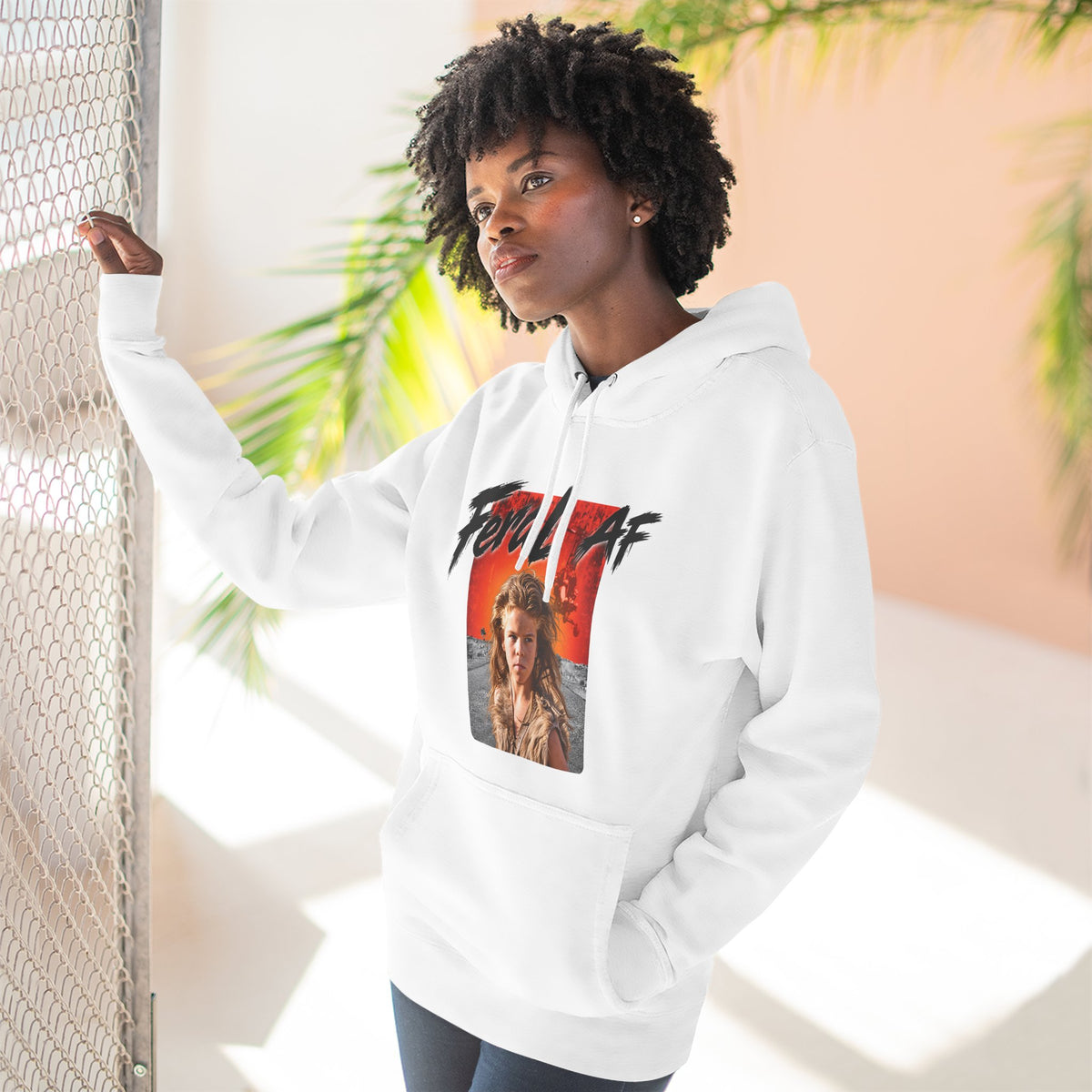 Woman wearing the White Feral AF hoodie indoors beside a palm, fiery wasteland print on her chest