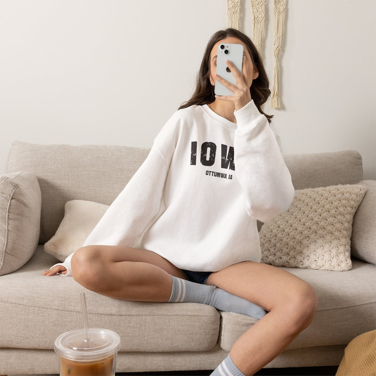Woman relaxing on a sofa in the white Iowa sweatshirt printed IOWA over OTTUMWA IA