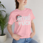 Woman in the Pink Retired As Fuck tee and jeans standing beside a houseplant