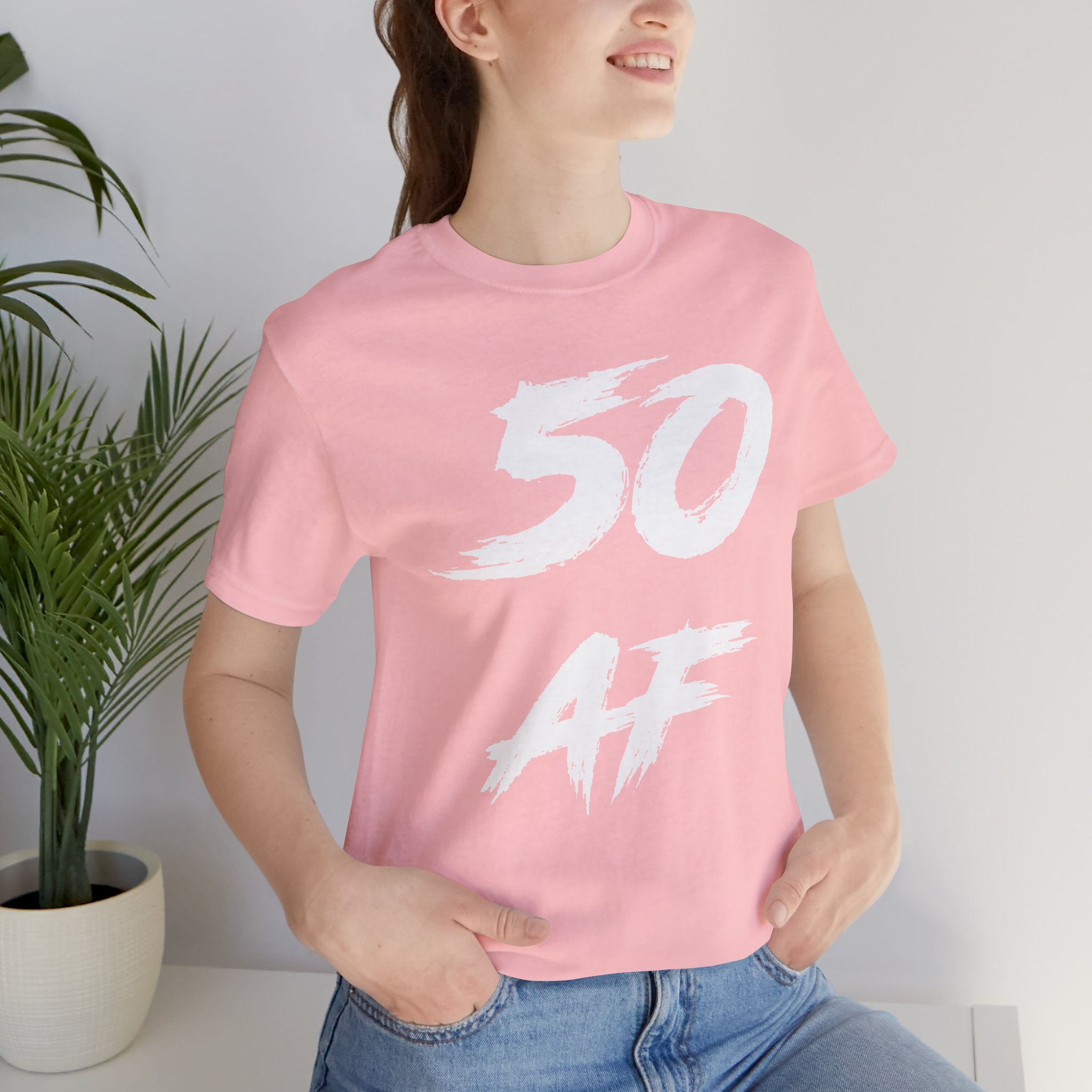 Woman indoors by a plant wearing the pink 50 AF birthday tee