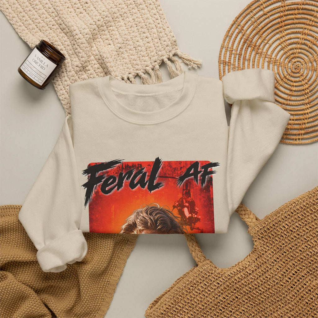 Sand Feral AF sweatshirt folded on a woven mat with a knit throw and a candle