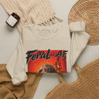 Sand Feral AF sweatshirt folded on a woven mat with a knit throw and a candle