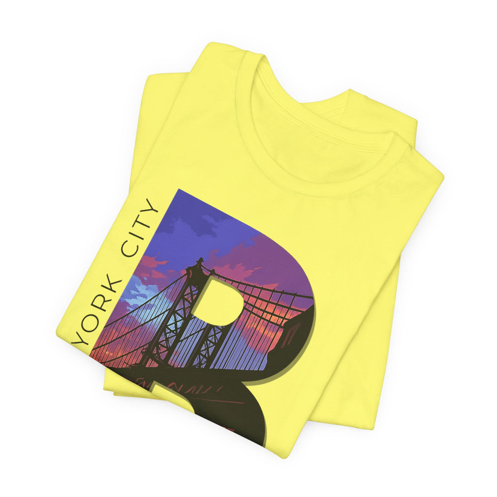 Yellow t-shirt folded in a stack, close-up of the oversized 'B' with a Brooklyn Bridge sunset skyline graphic