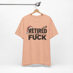 Heather Peach Retired As Fuck T-shirt hanging on a wooden hanger against a plain wall