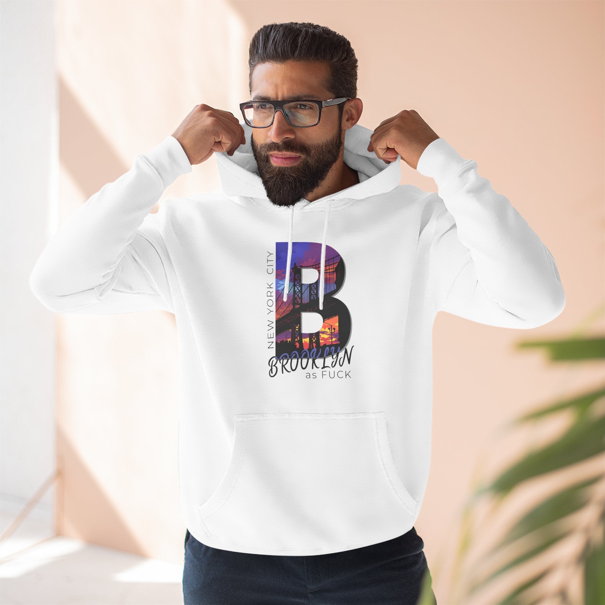 White hoodie worn by a bearded male model adjusting his hood, close-up chest view, with the 'B' Brooklyn skyline graphic.
