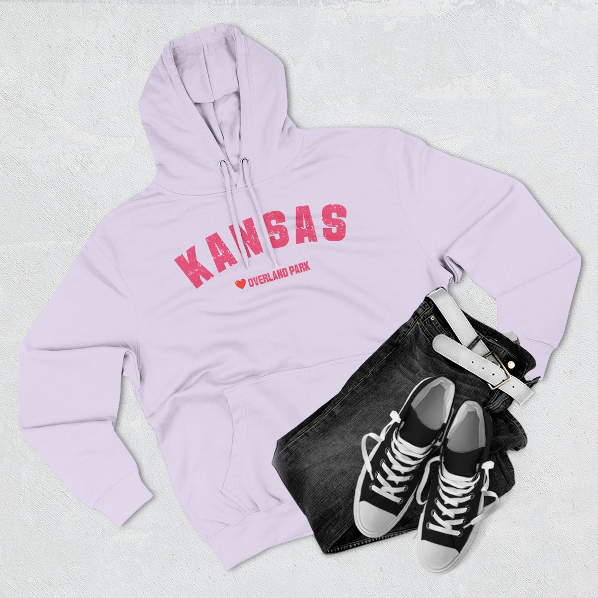 Lilac Kansas hoodie styled flat with denim and trainers, pink varsity KANSAS over a heart and OVERLAND PARK