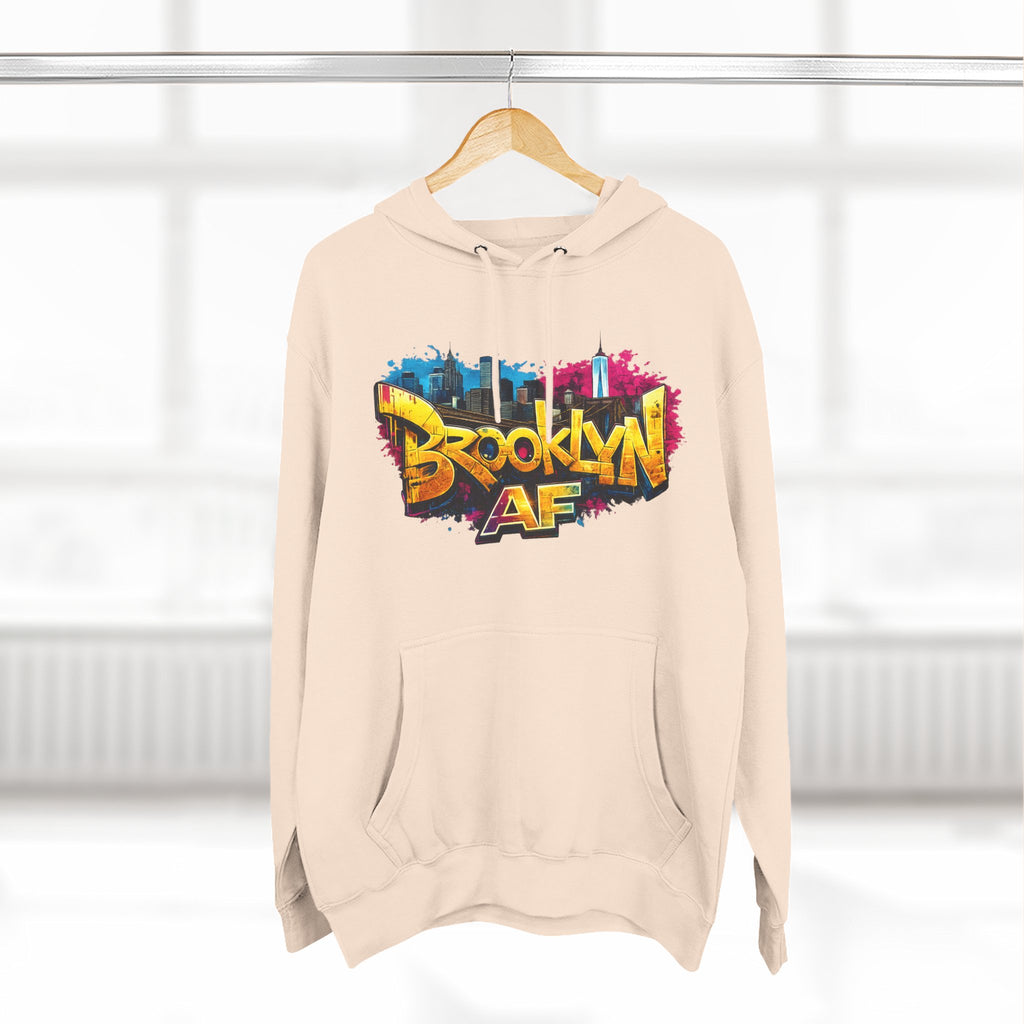 Sandshell hoodie hanging on a wooden hanger, showing the colorful graffiti-style Brooklyn AF skyline print.