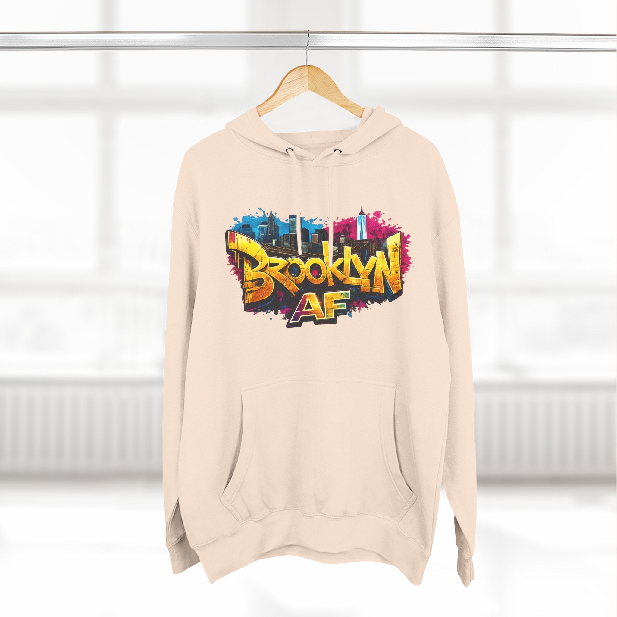 Sandshell hoodie hanging on a wooden hanger, showing the colorful graffiti-style Brooklyn AF skyline print.