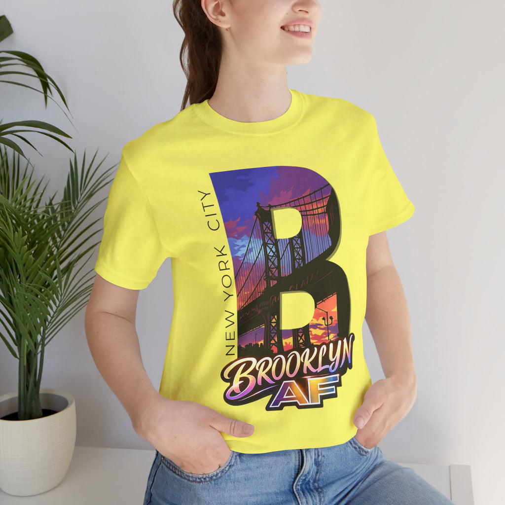 Yellow t-shirt worn by a model, close-up of chest print showing the 'B' with Brooklyn Bridge sunset skyline graphic
