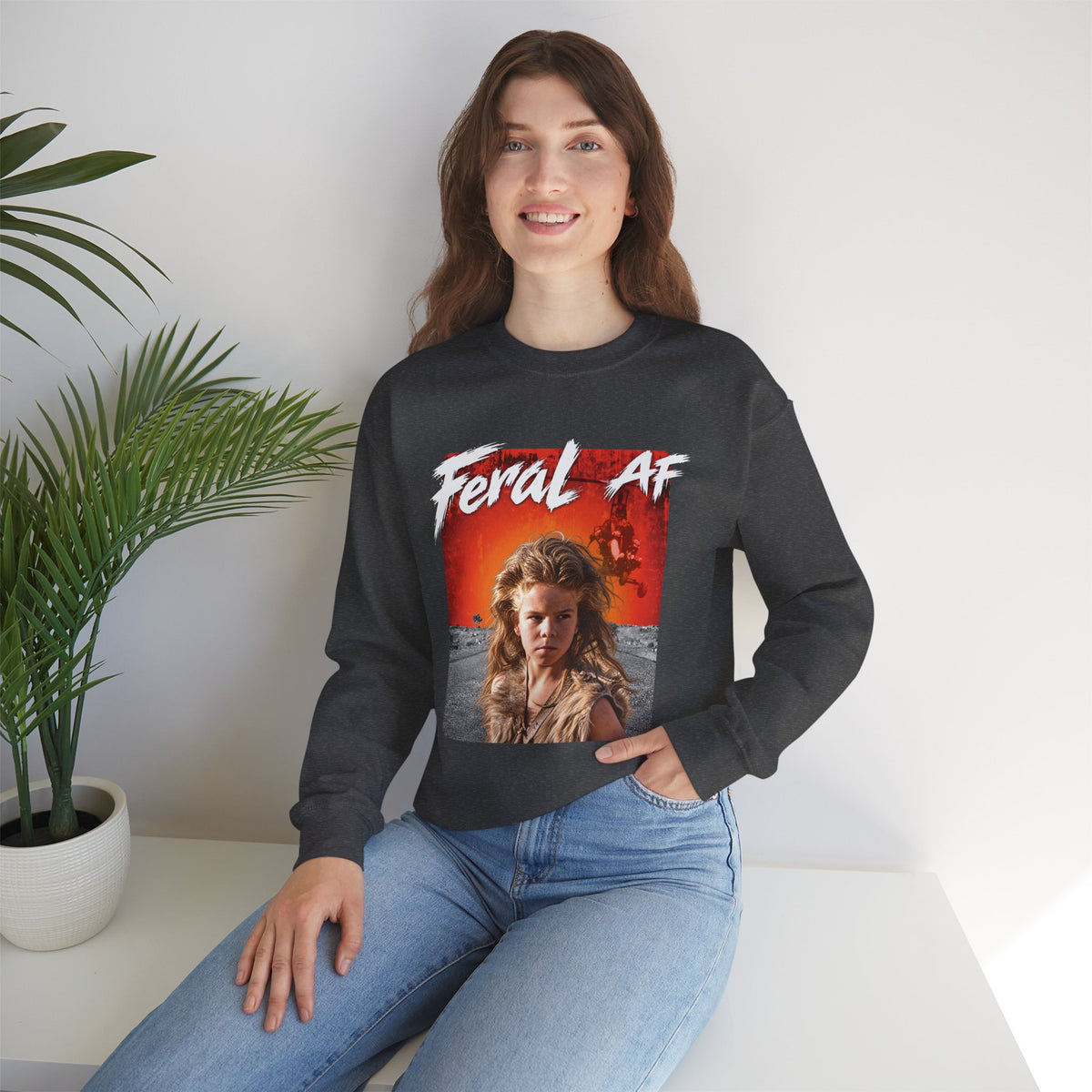 Woman seated by a potted palm in the Dark Heather Feral AF sweatshirt, front print showing