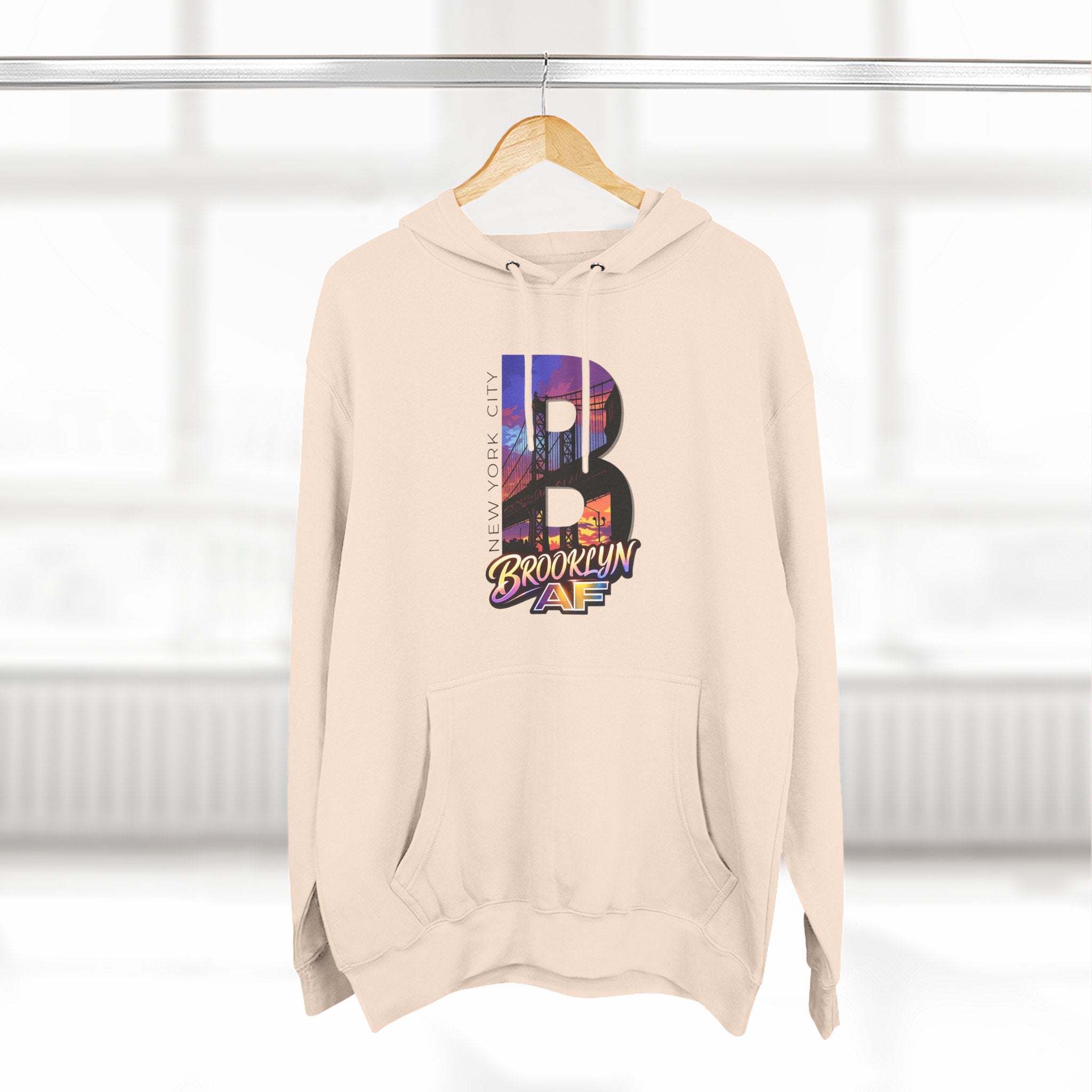 Oatmeal heather hoodie hanging on a wooden hanger, bold B with a Brooklyn Bridge sunset skyline graphic and Brooklyn AF logo.