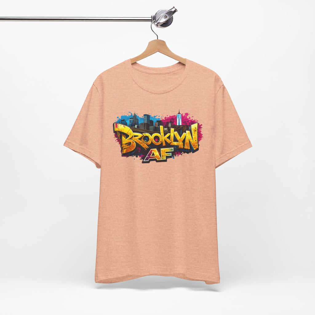 Heather Peach t-shirt on a wooden hanger, front view, with graffiti-style Brooklyn AF lettering over a skyline splash.